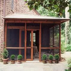 an outdoor covered patio with potted plants on the ground and brick building in the background