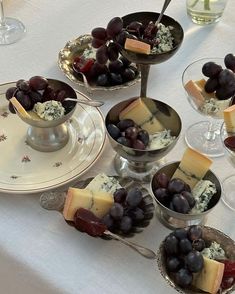 grapes, cheese and crackers are arranged in bowls on a table with wine glasses