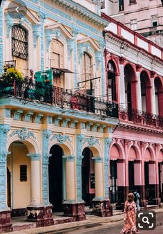 two people walking down the street in front of colorful buildings with balconies and balconyes