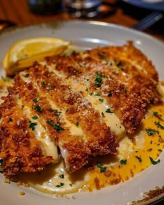 a white plate topped with meat covered in sauce and cheese next to lemon wedges