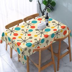 a table and chairs are covered with a multicolored flower design, next to a potted plant