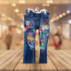 a pair of jeans with colorful patches on them sitting on top of a wooden table