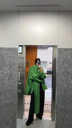 a woman is standing in an elevator talking on her cell phone while wearing a green shawl