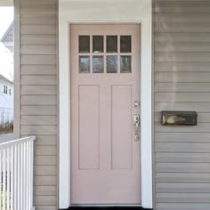 a pink front door on a gray house with white railings and two sidelights