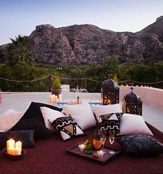 an outdoor patio with candles, pillows and wine glasses on the table next to it