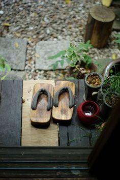 two pairs of sandals sitting on top of a wooden table next to potted plants