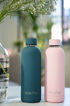 two water bottles sitting next to each other on a table with flowers in the background