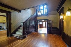 an empty room with wooden floors and stairs leading up to the second floor, along with two large windows