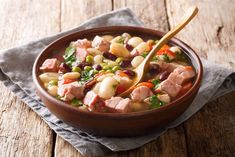 a bowl of soup with beans, ham and vegetables on a wooden table stock photo