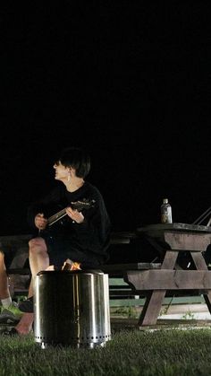 two people sitting on a bench at night with one playing an electric guitar and the other singing