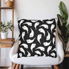 a black and white pillow sitting on top of a chair next to a potted plant