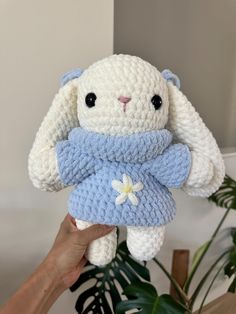 a white and blue stuffed animal with a flower on it's chest is held up by a hand