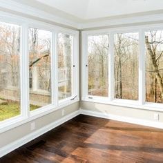 an empty room with wood floors and large windows looking out onto the woods outside on a sunny day