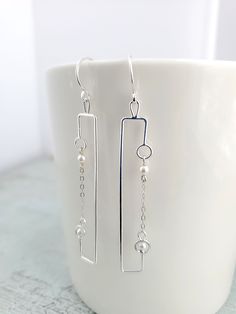 "These Silver and Mother of Pearl Earrings are a loose interpretation of the electrical circuit diagram.  The simple geometric design offers a minimalist elegance to any ensemble. Disclaimer: not meant to be scientifically loyal because aesthetics before accuracy MATERIALS:  - silver-plated or sterling silver wire (including the ear wire)  - Shell pearls or Mother of Pearl  - silver plated or sterling silver chain  - 6.5 cm in length (from top of ear wire to bottom of earring) SILVER PLATE vs ST Modern Linear Earrings For Anniversary, Minimalist White Gold Linear Earrings For Anniversary, Modern White Gold Linear Earrings For Anniversary, Modern Pierced Linear Earrings For Anniversary, Modern Linear Pierced Earrings For Anniversary, Modern Hypoallergenic Linear Earrings, Modern Sterling Silver Linear Earrings For Anniversary, Modern Rectangular Earrings For Anniversary, White Modern Jewelry With Simple Design