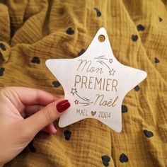 a hand holding a wooden star ornament that says mom, premer noel