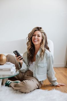 a woman sitting on the floor holding a cell phone and smiling at the camera,