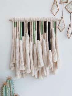 a white wall hanging with tassels on it next to a cacti