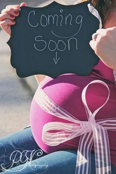 a pregnant woman holding up a chalk board with the words coming soon written on it