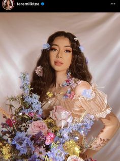 a woman with flowers in her hair is holding a bouquet of blue and pink flowers