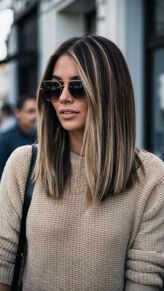 This image features a straight medium-length brunette balayage with blonde highlightsThe sleeksmooth finish showcases the contrast between the darker roots and lighter tipsadding a modern twistThe clientwearing sunglasses and a light sweateris set against an urban backdropmaking this style perfect for a chiccity lookIdeal for clients with an oval or square face shapethis style is both stylish and low-maintenance. Hair Low Lights Brunette, Grow Out Highlights Blondes, Low Maintenance Hair Color Brunette Fall, Low Maintenance Brunette Highlights, Brunette Roots Blonde Hair, Fall Hair With Blonde Highlights, Low Lights And Highlights Blonde Fall, Dark Brunette Hair Ideas, Medium Length Brunette Balayage