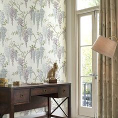 a wooden desk sitting next to a window covered in curtains and a lamp on top of it