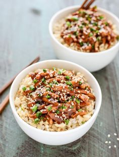 two white bowls filled with rice and meat covered in sesame seeds, garnished with green onions