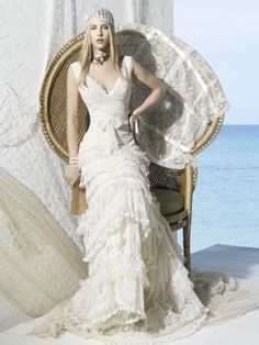 a woman in a white dress is sitting on a chair by the ocean and posing for a photo