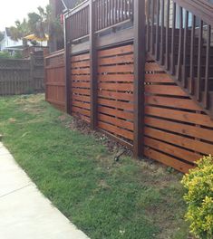 a wooden fence in front of a house with grass and bushes on the side walk