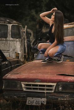 a woman sitting on the hood of an old rusted car in a junk yard