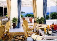 a living room filled with lots of furniture next to a large open window covered in blue drapes