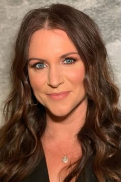 a woman with long brown hair and blue eyes posing for a photo in front of a wall