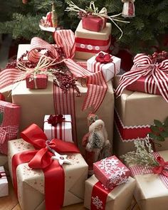 many wrapped presents under a christmas tree with red and white bows on them, all stacked together