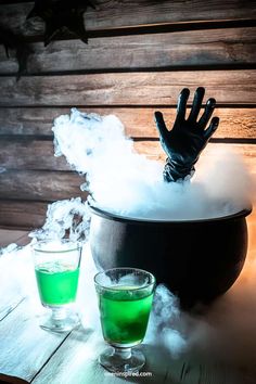 two glasses with green liquid in them sitting on a table next to a black pot