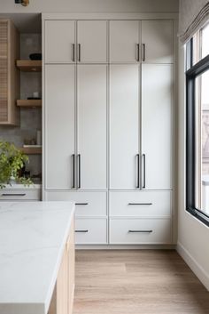 a kitchen with white cabinets and wood flooring next to a large window in front of it