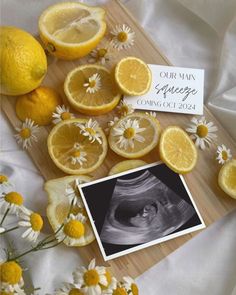 an arrangement of lemons and daisies on a wooden cutting board with a card