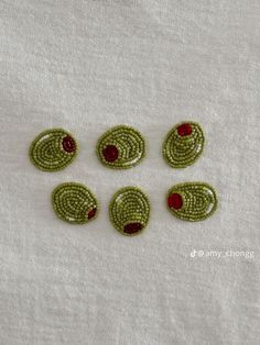 six green and red beaded buttons sitting on top of a white cloth