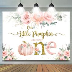 a white wall with pink flowers and gold lettering on it that says our little pumpkin is turning one