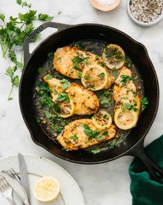 chicken with lemons and parsley in a skillet on a marble counter top