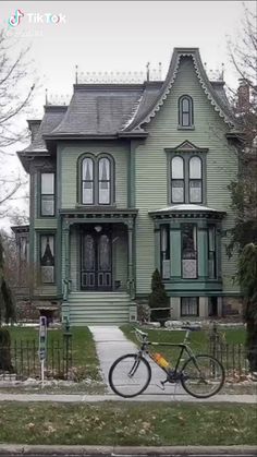 a bike parked in front of a green house on a street with trees and bushes