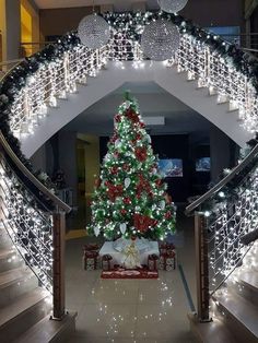 a decorated christmas tree sitting in the middle of a hallway next to some banisters