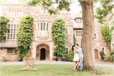 a man and woman standing next to a tree in front of a large brick building