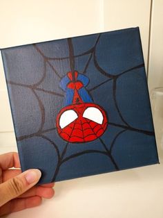 a hand holding up a small canvas with a spider man on it's face