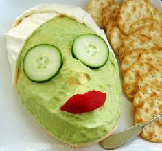 a face made out of cucumber and crackers on a plate next to crackers