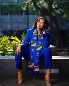 a woman sitting on a bench wearing a blue suit and yellow scarf with gold letters