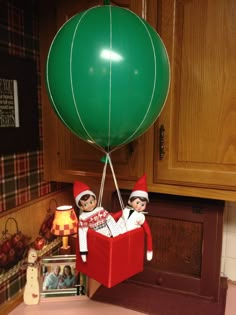 two elfs are in a red box with a green balloon attached to the top