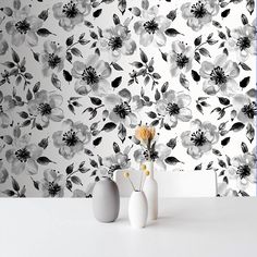 two vases with flowers in front of a wallpapered background that has black and white flowers on it