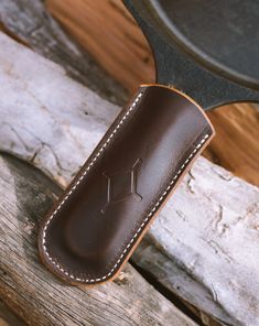 a leather knife case sitting on top of a piece of wood next to a frying pan