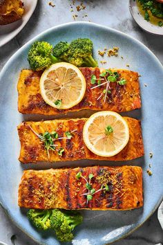 salmon and broccoli on a blue plate with lemons, parsley and herbs