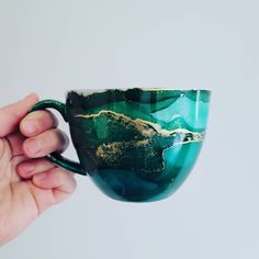 a hand holding a green and gold coffee cup