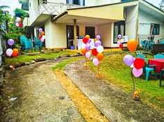 some balloons are on the ground in front of a house with lawn chairs and tables